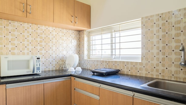 A kitchen with wooden cabinets, a microwave, a scale, and a window with blinds.