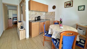 A compact kitchen with wooden cabinets, a tiled backsplash, and a dining area with a table and chairs. - Apartment Zlatica - 530 m from sea, private terrace, garden view, private parking, BBQ (Šilo)