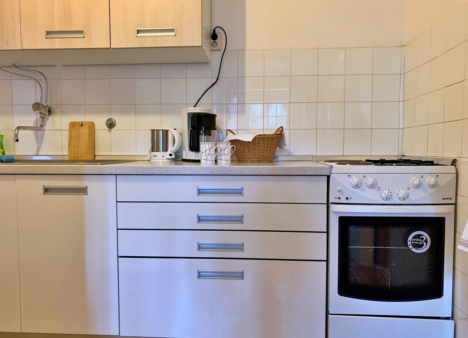 Eine Küche mit weißen Schränken, einem Herd, einer Kaffeemaschine und einem Wasserkocher.