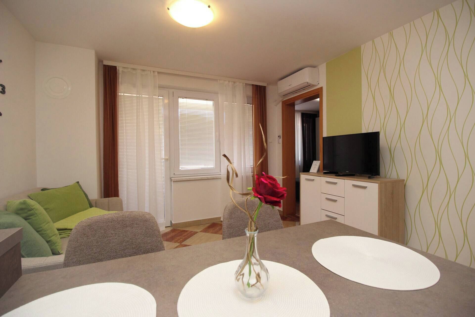 Una sala de estar con un sofá, una mesa de centro con un jarrón y un televisor sobre un mueble.
