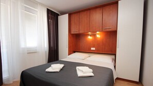 A hotel room with a bed, wooden headboard, and a window with curtains. - Apartment Brnic AQ 3 - with Balcony, 90 m from the Beach (Baska)