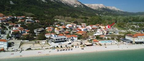 A coastal town with buildings, a beach, and mountains in the background.