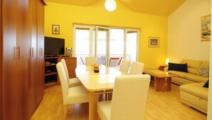 A living room with a wooden dining table, white chairs, a sofa, and a television.