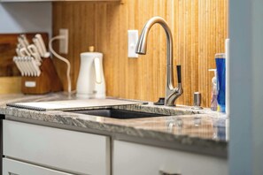 A kitchen with a stainless steel faucet, a wooden backsplash, and a granite countertop.