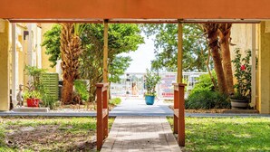 Une allée couverte avec un banc, entourée de verdure et de plantes en pot.