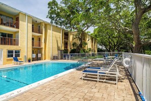 A swimming pool with lounge chairs and a fenced deck area, surrounded by a yellow building with balconies. - ‼️Calm Waterside Condo‼️ | Kayaks, Paddles, Pool (Mary Esther)