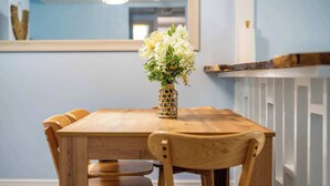 Une table à manger en bois, sur laquelle est posé un vase de fleurs, entourée de chaises en bois.