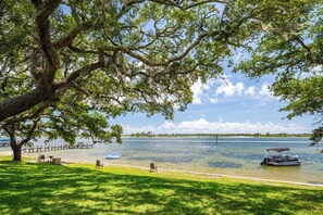 A lakeside park with a large tree, picnic tables, and a boat on the water.