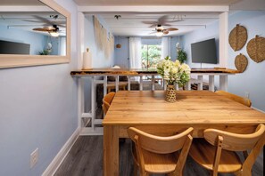 A dining area with a wooden table, four chairs, a vase with flowers, a television, and decorative wall art.
