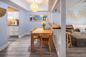 A modern kitchen with white cabinets, a wooden dining table, and a hanging light fixture.
