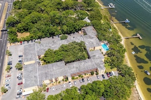 An aerial view of a parking lot adjacent to a building with a large green area and a beach.