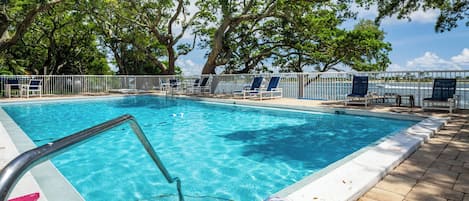 A swimming pool with clear blue water, surrounded by lounge chairs and a white fence.