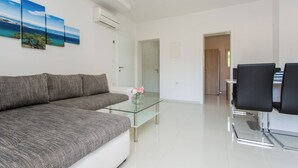 Una sala de estar moderna con un sofá gris, una mesa de centro de cristal y un comedor con sillas negras.