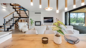 Una sala de estar moderna con una escalera de madera, un televisor de pantalla plana y un ventanal con vistas a la vegetación.