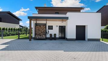 Situated on a paved area, this building features a covered porch with firewood and potted plants.