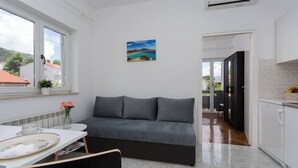 Un salon moderne avec un canapé gris, une table à manger ornée d’une assiette à motifs floraux et un tableau représentant un paysage côtier.