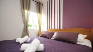 Un lit bien fait, avec une literie violette et des serviettes blanches, une tête de lit en bois et un mur à rayures en arrière-plan.