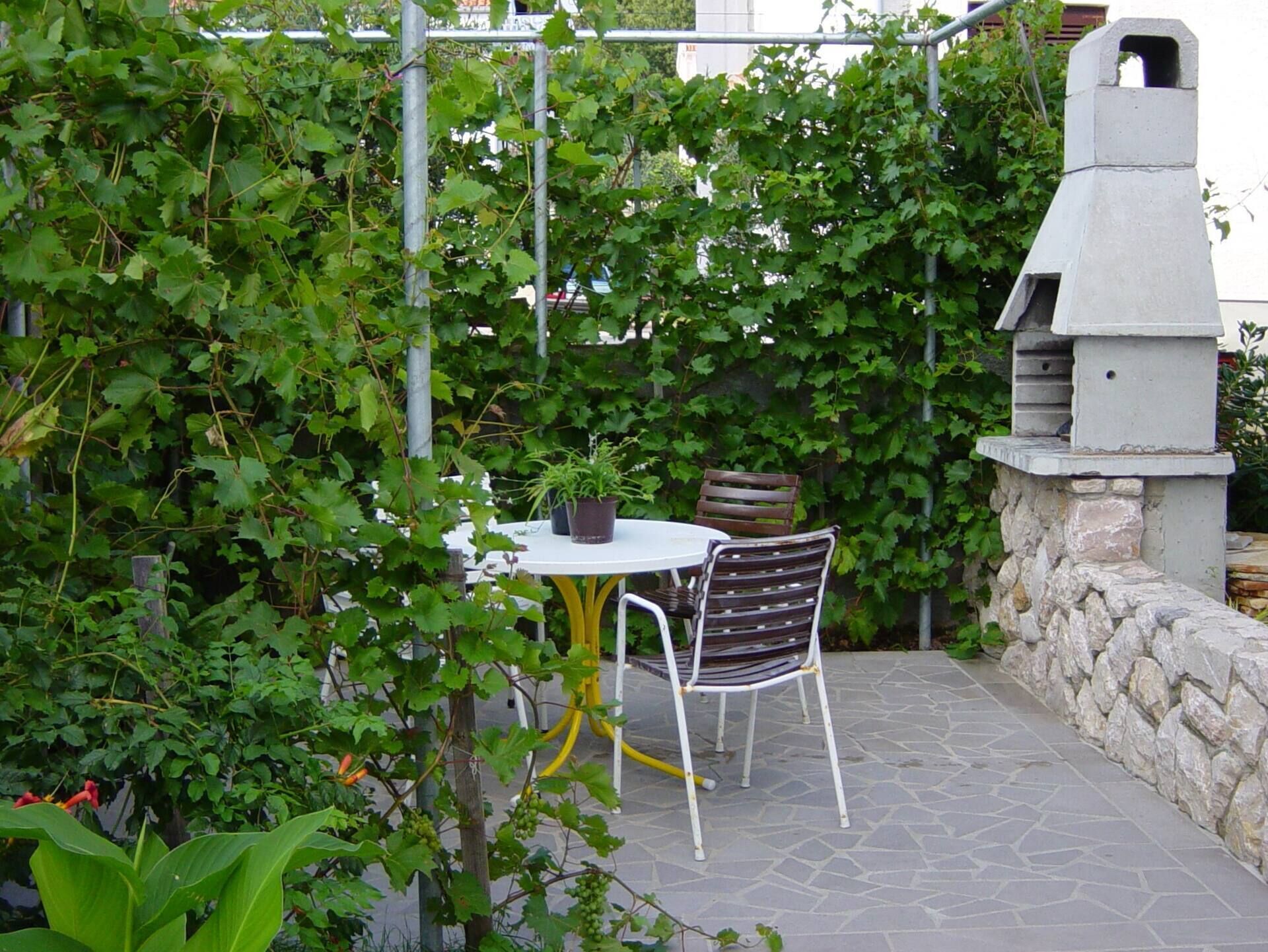 An outdoor patio with a stone floor, a round table, two chairs, and a grill structure.
