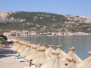 Une plage avec des parasols en paille et des chaises longues blanches.