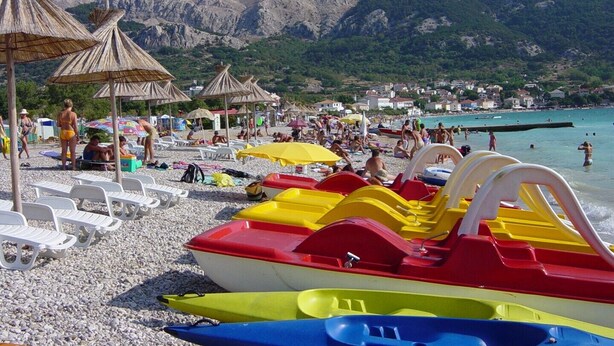 Une plage bordée de rangées de kayaks colorés, de parasols et de chaises de plage.