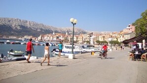 Un pueblo costero con un puerto deportivo, gente caminando y un ciclista.
