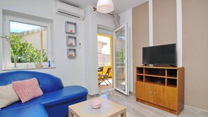 Una sala de estar moderna con un sofá azul, un televisor sobre un mueble de madera y una mesita con un cuenco rosa.