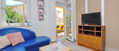 A modern living room with a blue sofa, a television on a wooden cabinet, and a small table with a pink bowl.