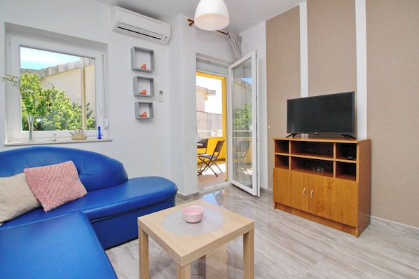 A modern living room with a blue sofa, a television on a wooden cabinet, and a small table with a pink bowl.