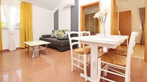Een woonkamer met een bank, een eettafel met stoelen en een vaas met bloemen.