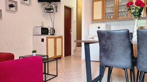A compact living space with a kitchenette, a dining area with two chairs, a TV mounted on the wall, and a small table with a plant. - Apartment Bugi PRIZ - on the Ground Floor, with Terrace (Baska)