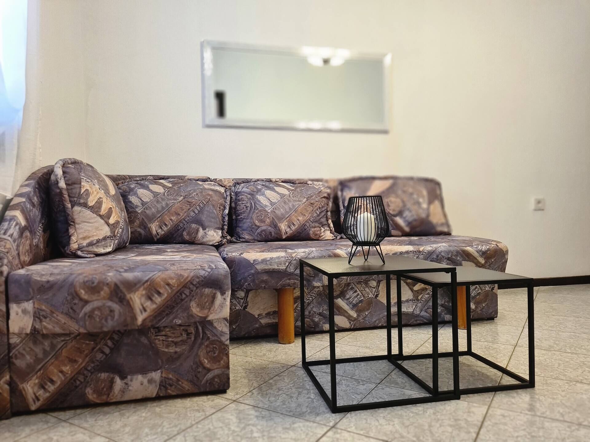 A living room with a patterned sofa, a small black coffee table, and a wall-mounted TV.