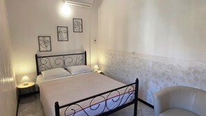 Un dormitorio con una cama, dos lámparas de noche, una silla y cuatro cuadros en la pared.