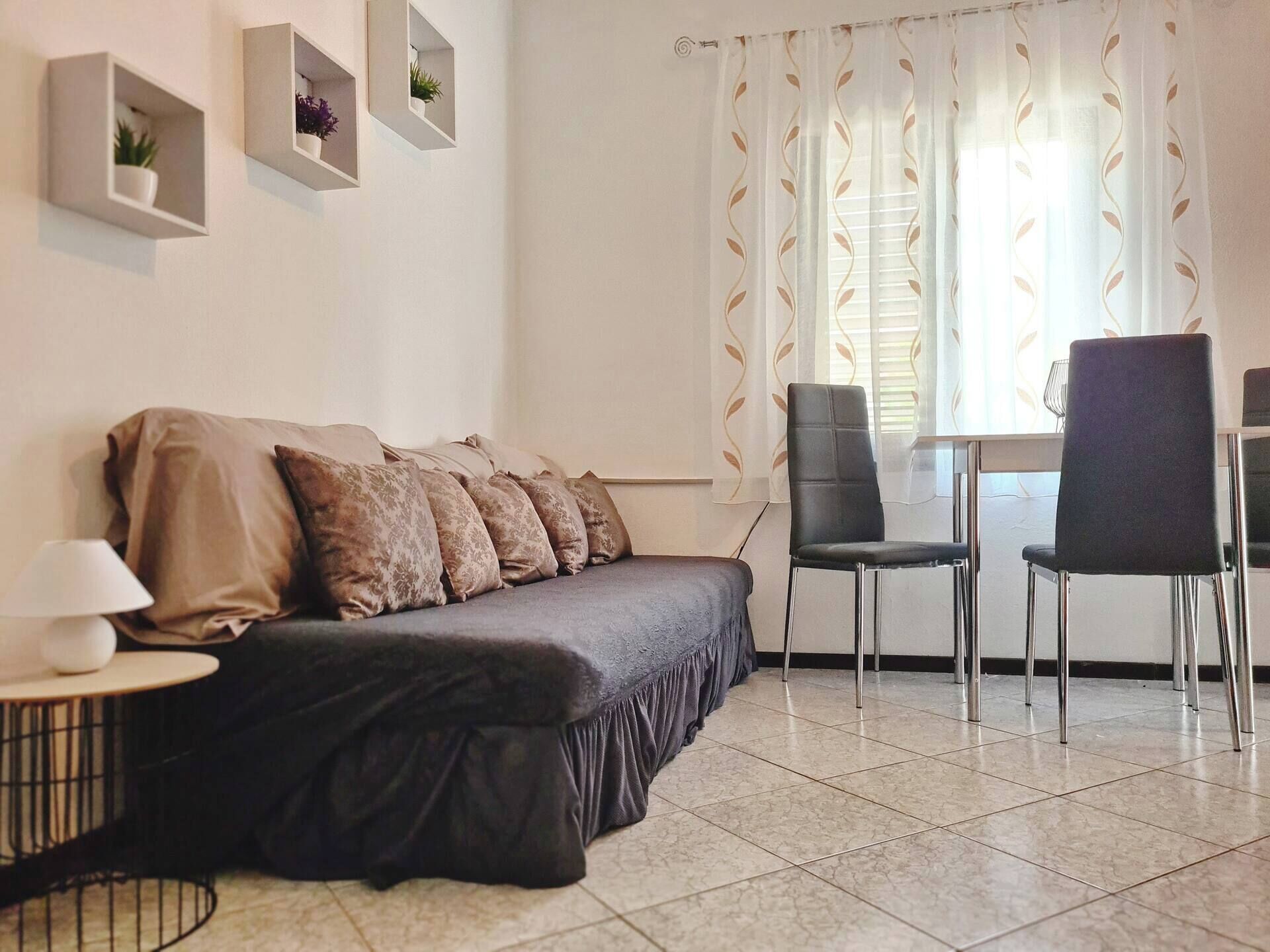 Una sala de estar moderna con un sofá, dos sillones, una mesita y una ventana con cortinas estampadas.