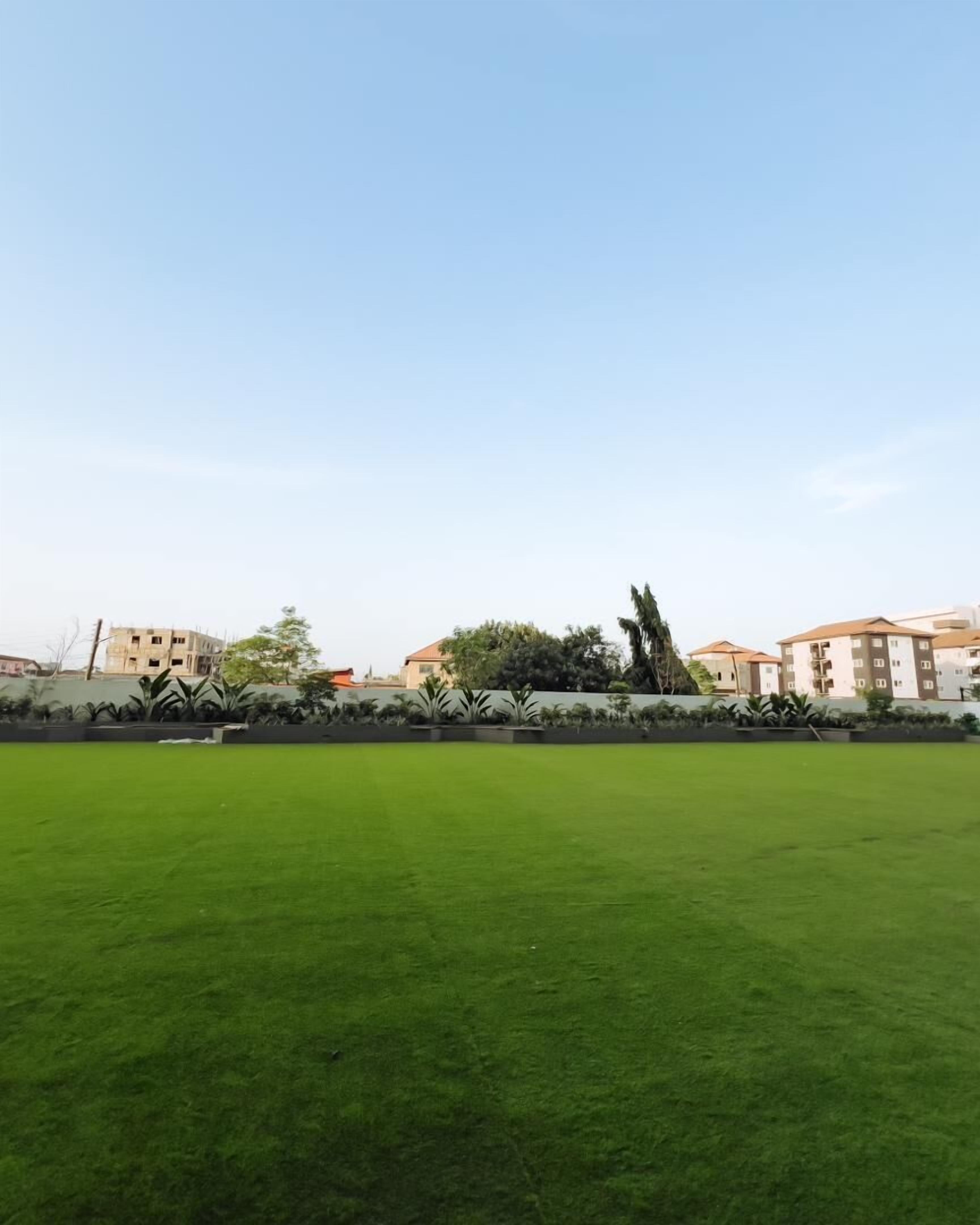 Una amplia zona verde con cielo despejado. En el fondo, varios edificios presentan una mezcla de estilos arquitectónicos.
