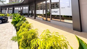 A C-Mart store with a modern building facade, large windows, and a paved walkway with green plants. - Meraki Homes at Loxwood House (Accra)
