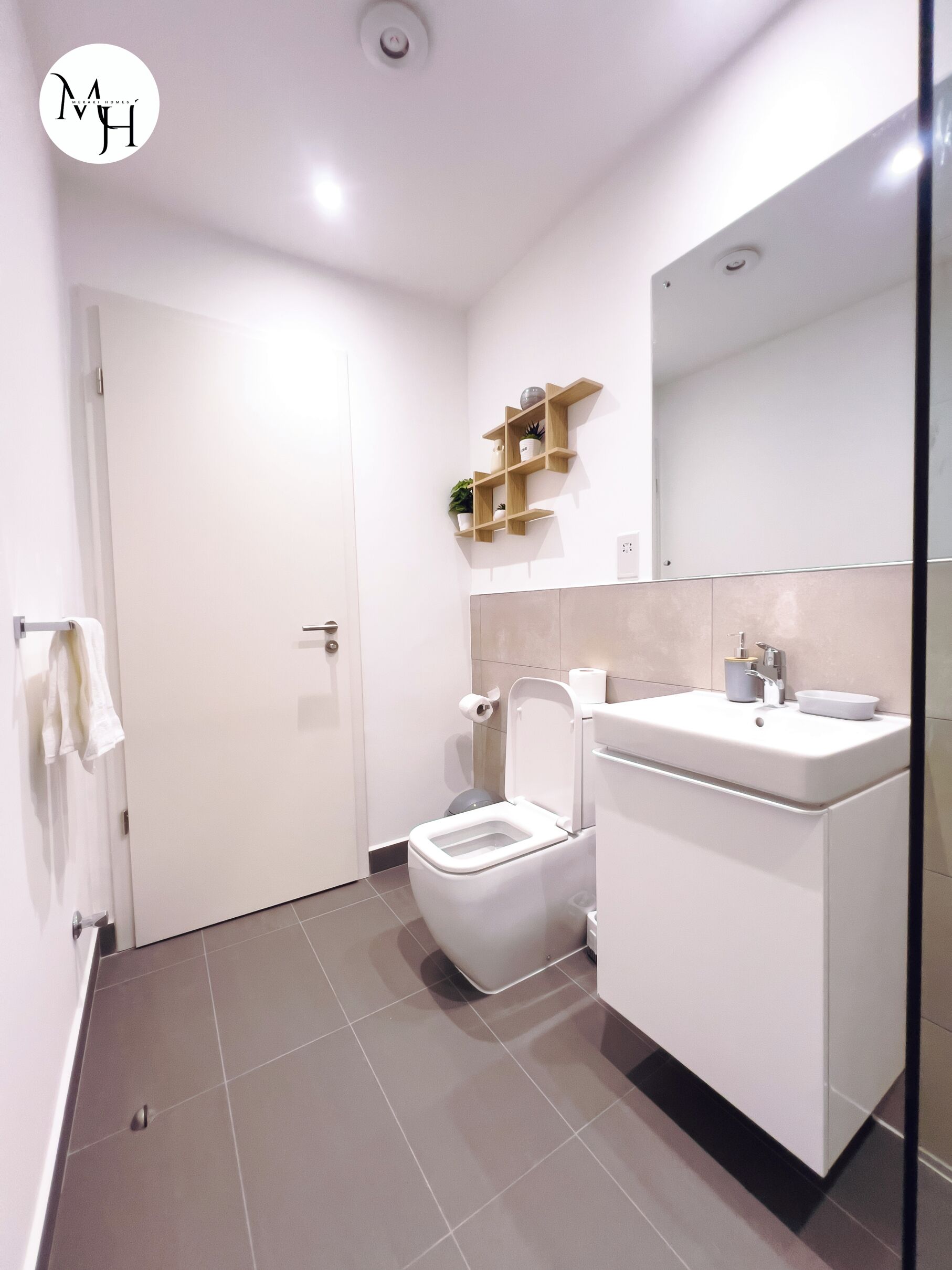 Een moderne badkamer met toilet, wastafel en spiegel. Daarboven hangen houten planken bij de wastafel en een handdoekrek aan de linkerkant.