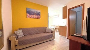 Un salon avec un canapé, un tableau accroché au mur et un téléviseur posé sur un meuble.
