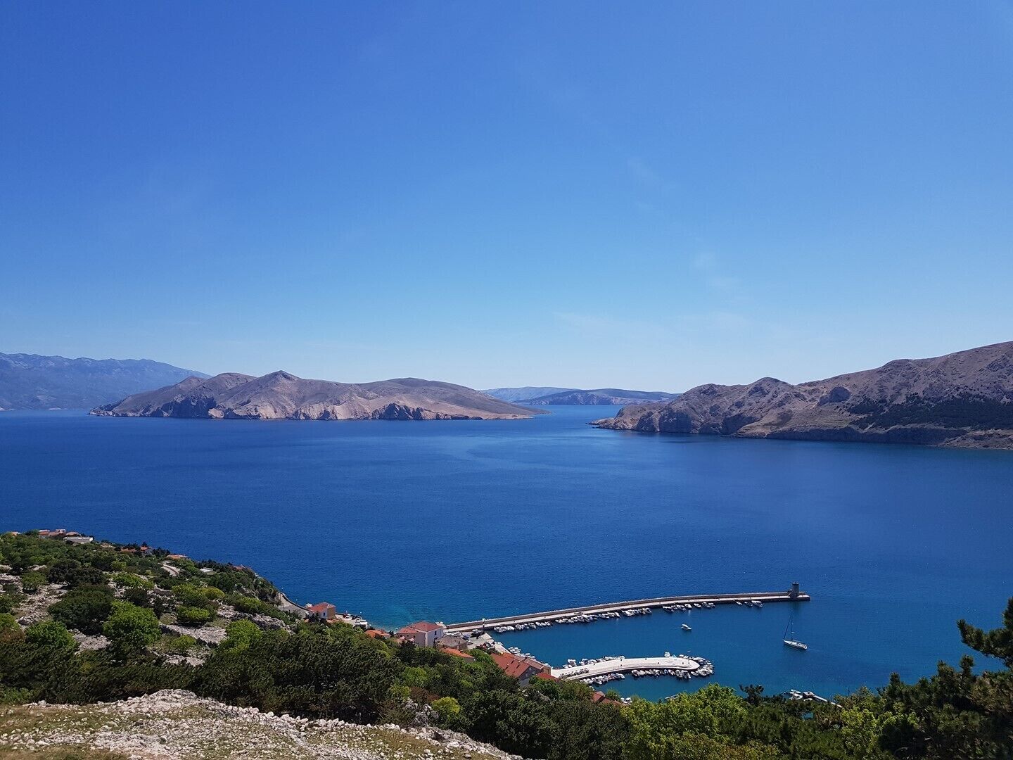 Een kustlandschap met een jachthaven, boten en een helderblauwe lucht.