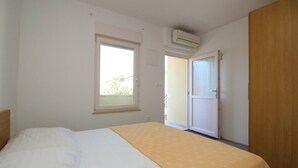 Quarto com cama, janela, ar-condicionado e porta para uma varanda.
