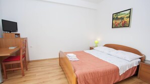 Un dormitorio con una cama de madera, un escritorio, una silla, un televisor y un cuadro en la pared.