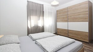 A bedroom with a bed, two pillows, a wooden wardrobe, and a window with curtains. - Apartment Mihaela - 350m from the Beach (Baska)