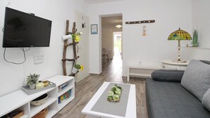 Una sala de estar con televisor, sofá, mesa de centro, estantería, pared decorativa con plantas y una lámpara.