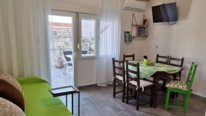 A room with a green sofa, a dining table with chairs, a TV mounted on the wall, and a sliding glass door leading to an outdoor area. - Apartment Fantov No.3 - with large Balcony, 250 m from the Beach (Baska)