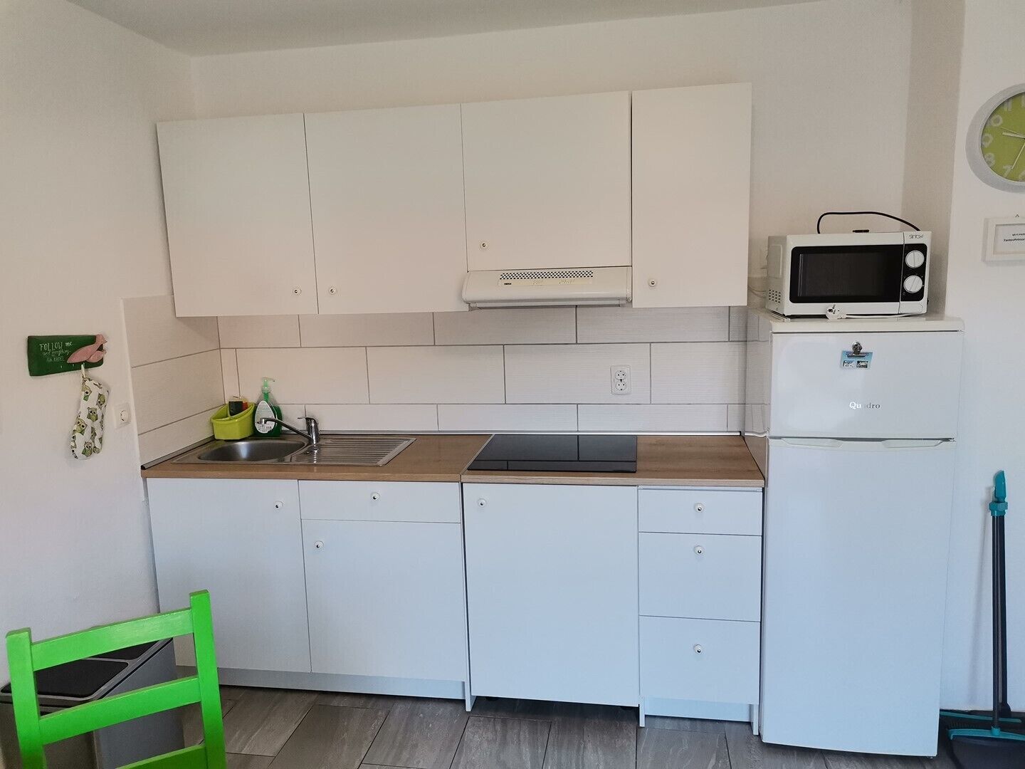 A compact kitchen with white cabinets, a microwave, a small refrigerator, a sink, and a green chair.