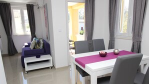 Ein modernes Wohnzimmer mit einer Couch, einem Esstisch mit Stühlen und einem durch einen offenen Durchgang einsehbarer Küchenbereich.