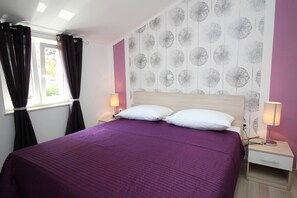 Un dormitorio con una cama, dos mesitas de noche, una ventana con cortinas y una pared con estampado floral.