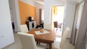 Un coin repas avec une table en bois, des chaises blanches et un téléviseur posé sur un meuble.
