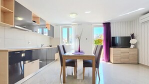 A modern kitchen with integrated appliances, a dining area with a table and chairs, and a living area with a TV and decorative items. - Apartment Gorica 2 No.1 - with Terrace and Pool (Baska)