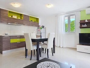 Eine moderne Küche mit weißen Schränken, einem Esstisch mit Stühlen, einem Flachbildfernseher und einem Fenster mit Vorhängen.