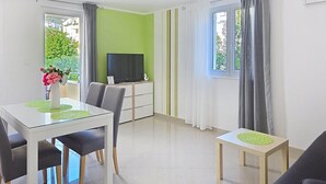 Een moderne woonkamer met een eetgedeelte, een televisie en uitzicht op groen.